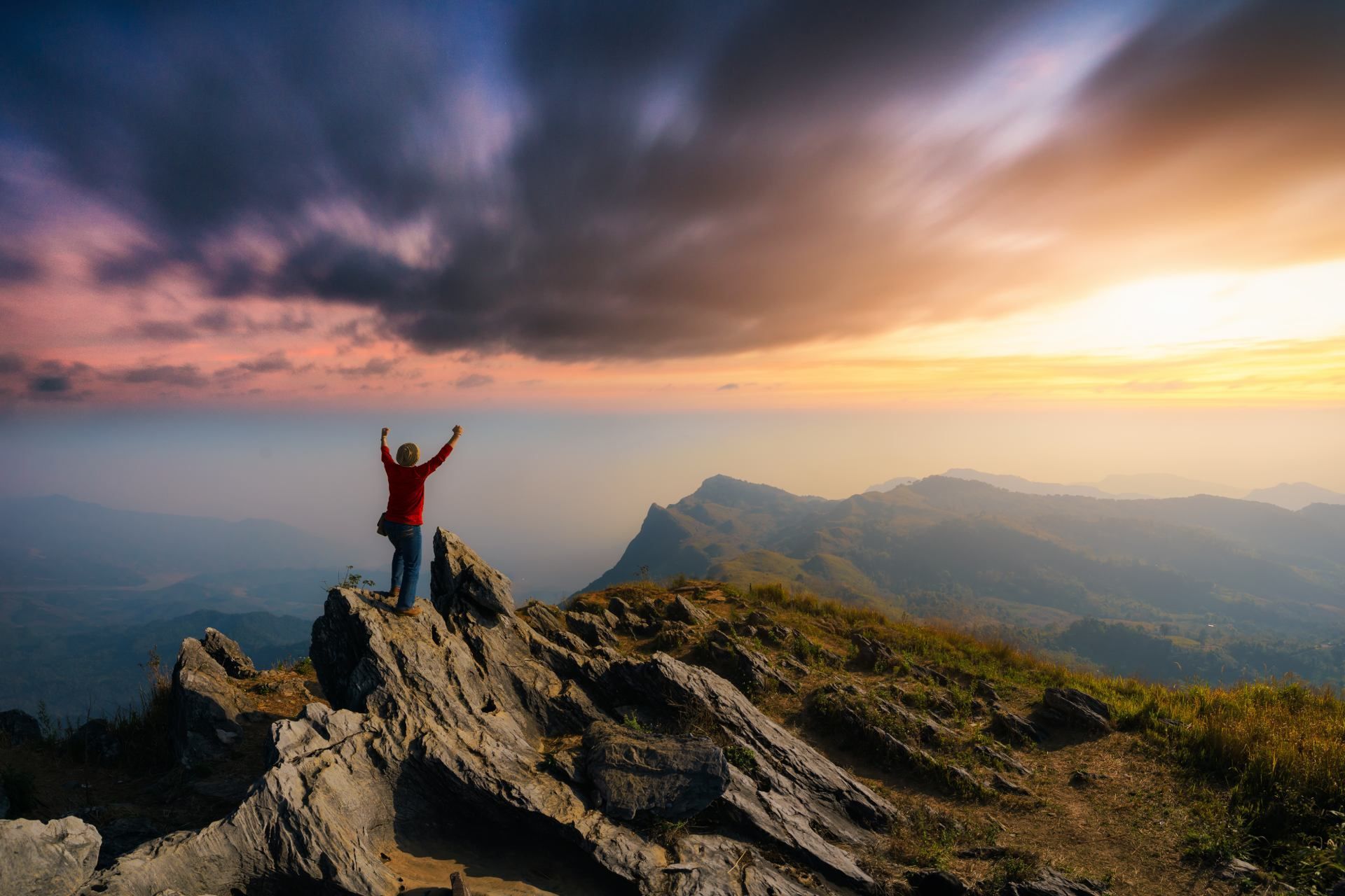 Eine Person steht mit erhobenen Armen auf einem Berggipfel.