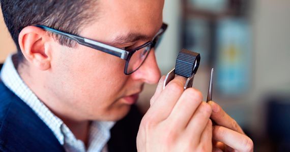 Un hombre que lleva gafas mira a través de una lupa un trozo de metal.