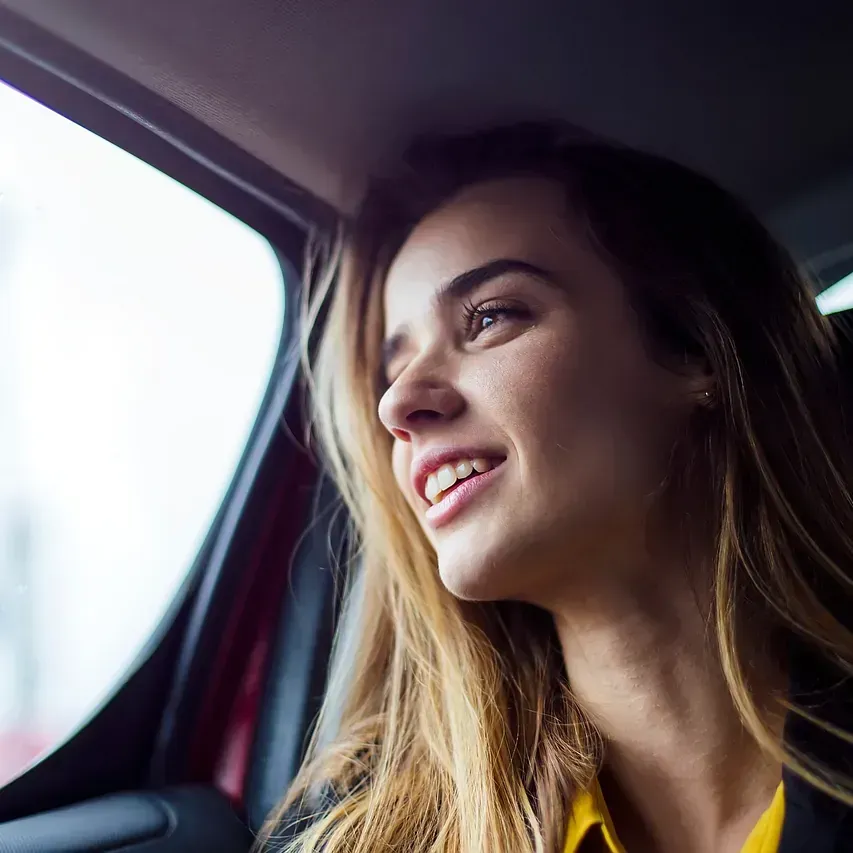 Una mujer sonríe mientras está sentada en el asiento trasero de un automóvil.