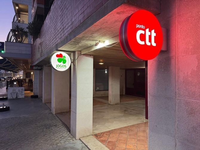 Entrada de um edifício com fachada de tijolos vermelhos, colunas brancas e uma placa vermelha à direita.