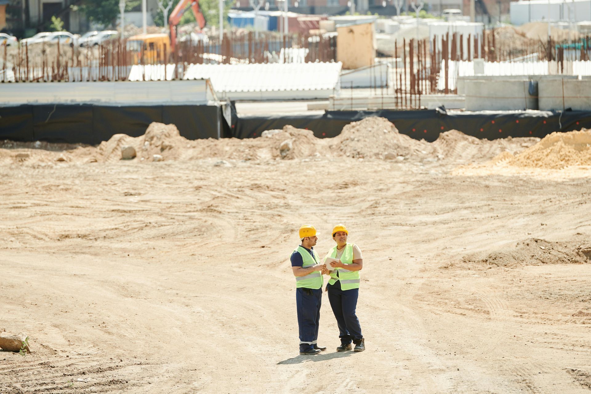 Un ouvrier du bâtiment portant un casque et un gilet de sécurité regarde un chantier de construction.