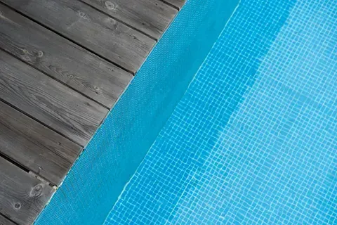 Hay una terraza de madera al lado de una piscina.