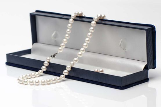 Eine edle Perlenkette liegt über einem Schmuckkästchen.
