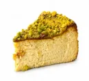 Una porción de tarta de queso cubierta de pistachos triturados sobre un fondo blanco