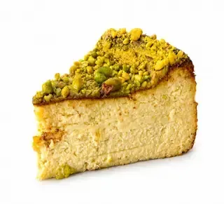 Una porción de tarta de queso cubierta de pistachos triturados sobre un fondo blanco