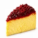Porción de tarta de queso amarilla cubierta con una brillante compota de frutos rojos, sobre un fondo blanco