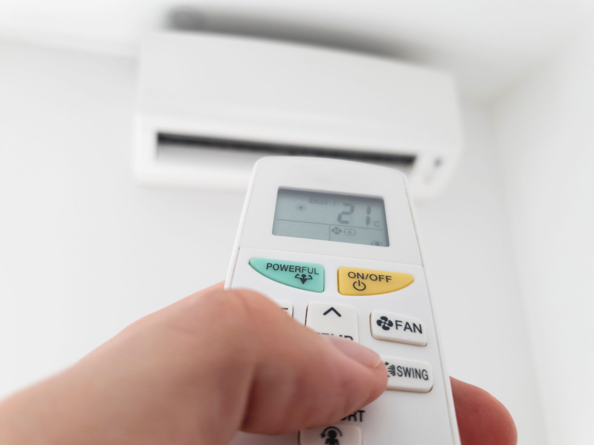 Eine Person hält eine Fernbedienung vor einer Klimaanlage.