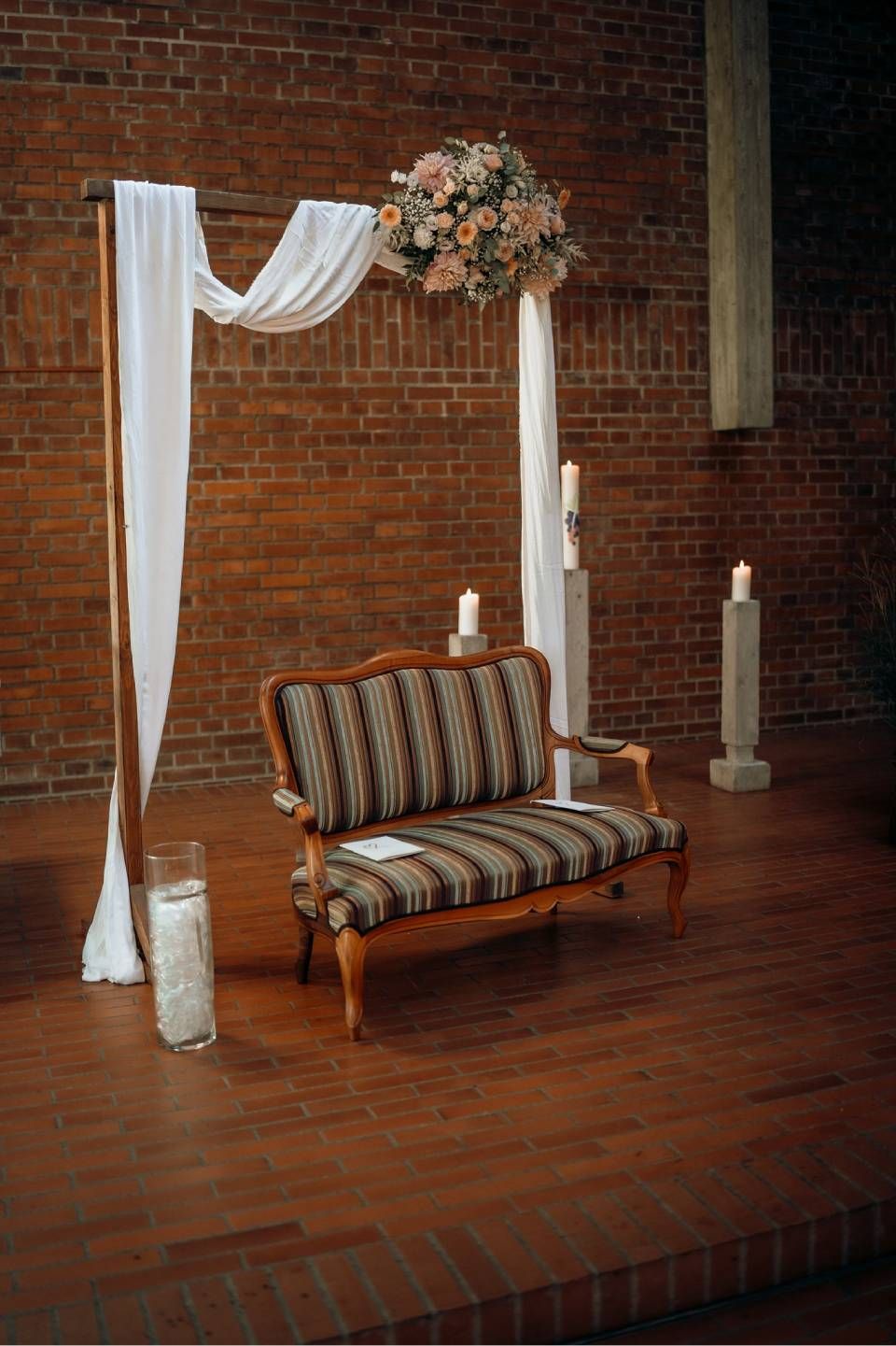 Auf einem hölzernen Podest steht ein gestreiftes Vintage-Sofa vor einem hölzernen Bogen, der mit weissem Stoff drapiert und mit Blumen geschmückt ist.