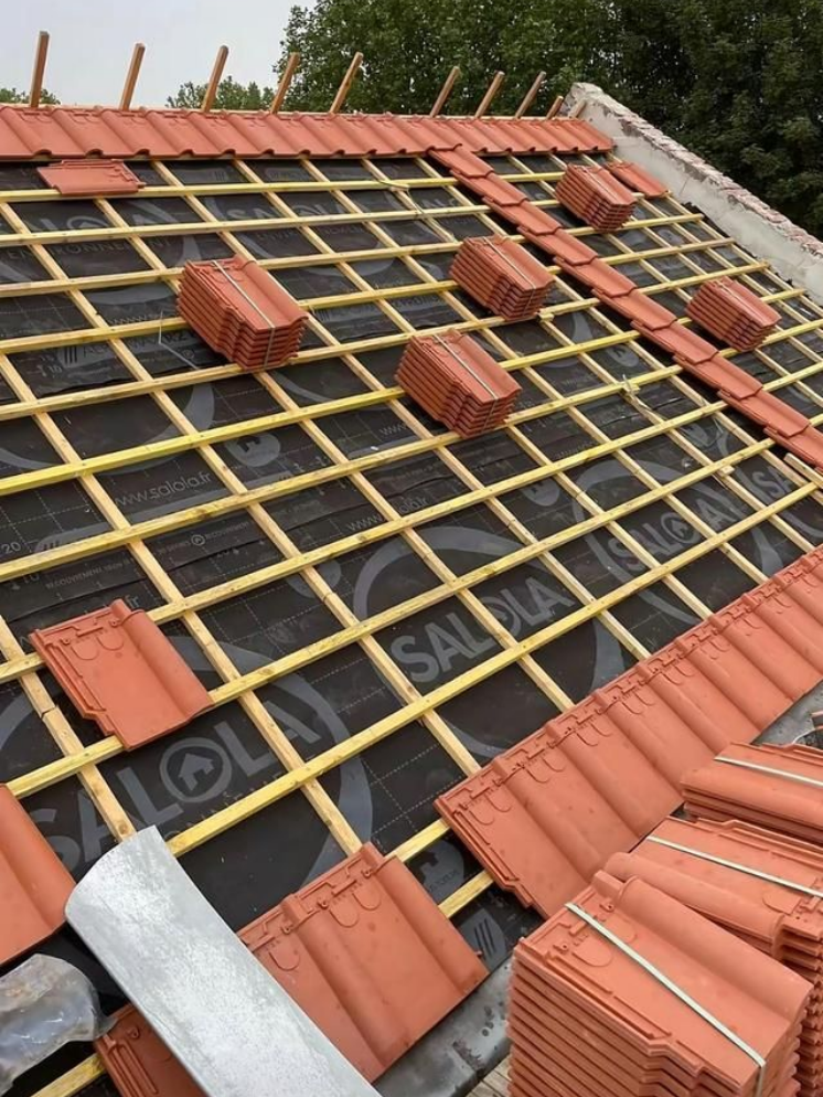 Toiture en cours de réalisation avec tuiles en terre cuite et charpente en bois.