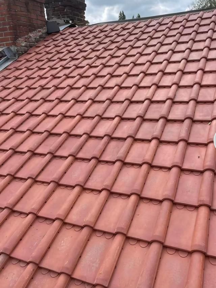 Toit de tuiles rouges sur un bâtiment, vue en angle, cheminée en arrière-plan, ciel couvert.