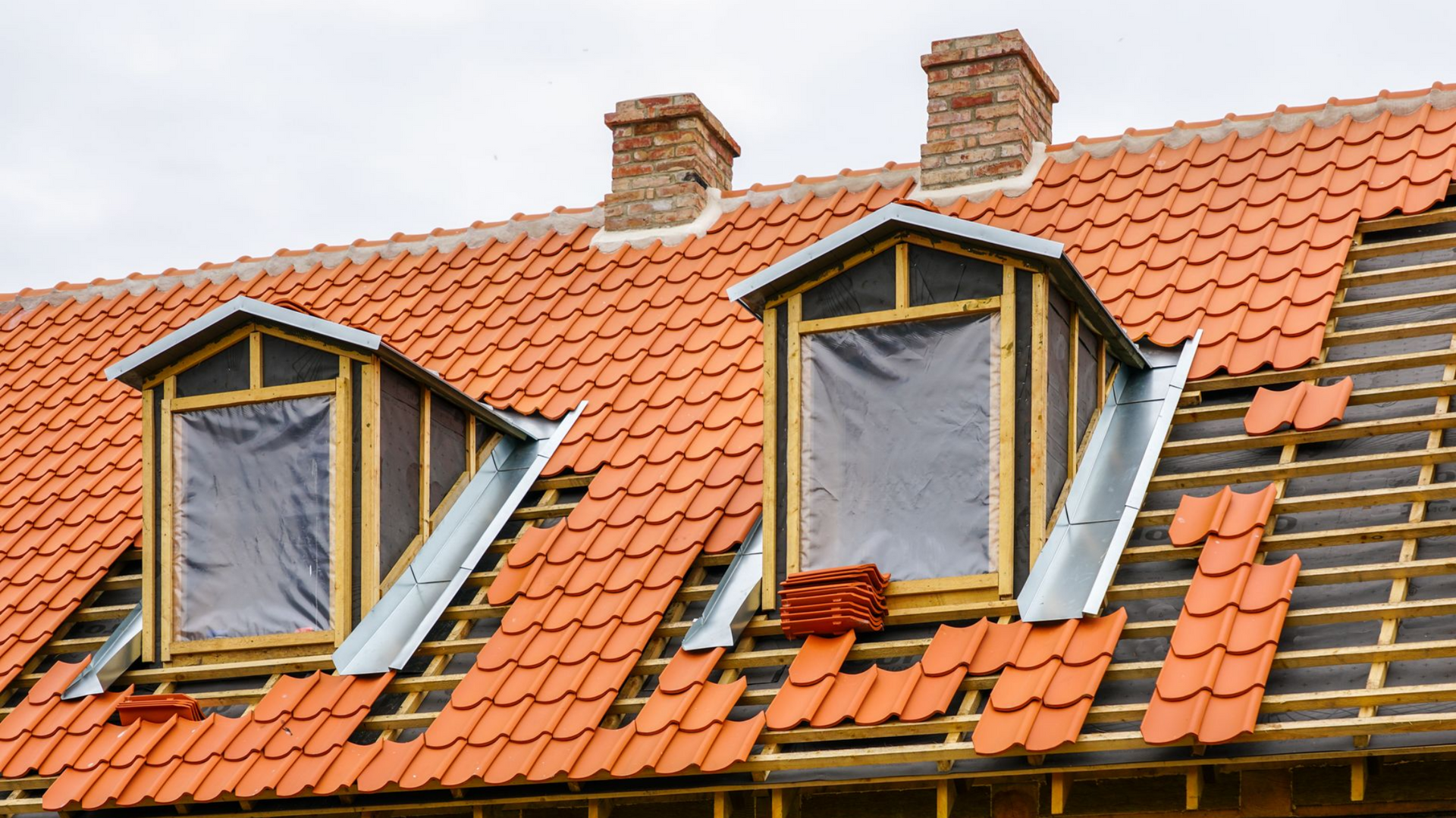 Toiture en tuiles rouges, avec deux lucarnes et deux cheminées. Réfection partielle en cours.