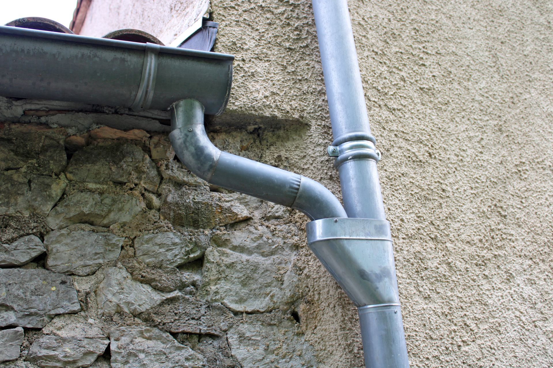 Système de gouttières grises sur un mur en pierre et en stuc.