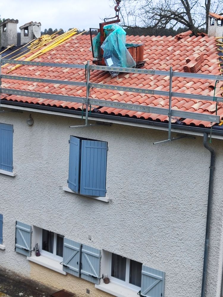 Un toit de maison avec des échafaudages, des tuiles rouges et des volets bleus, probablement en cours de rénovation.