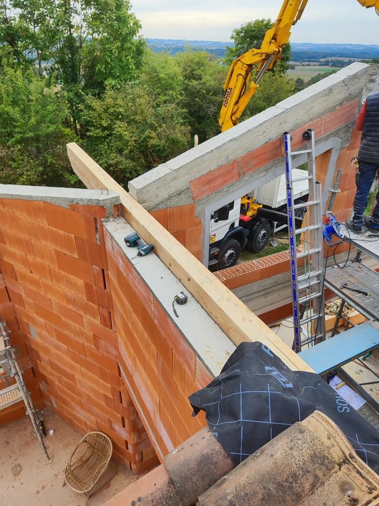Chantier : murs de briques, poutres en bois, béton et une excavatrice.