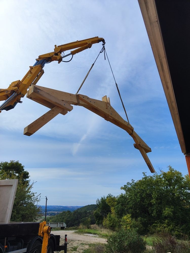 Une grue soulève une grosse poutre en bois ; chantier de construction, ciel ensoleillé.