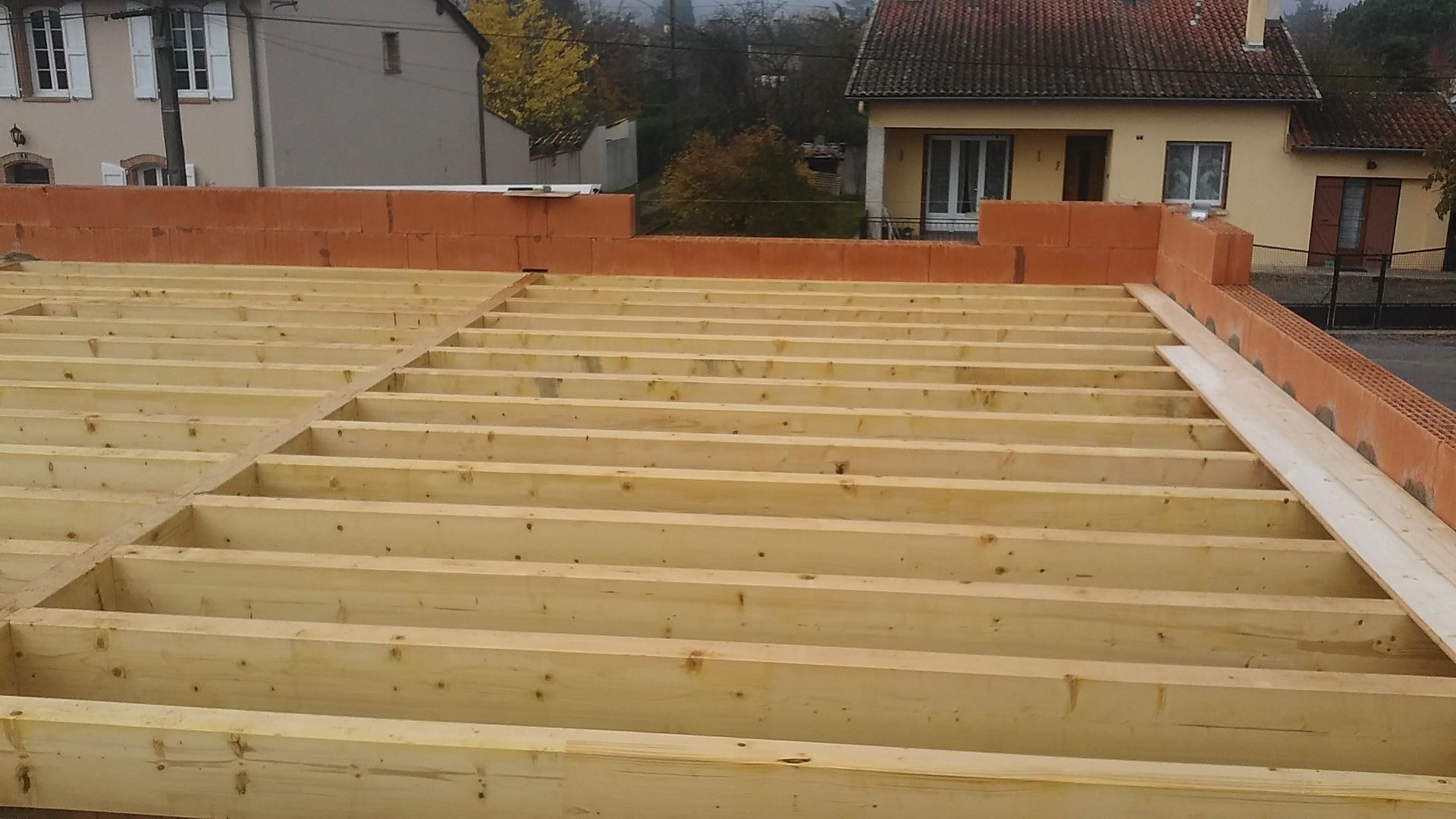 Poutres en bois disposées sur un chantier de construction, avec des maçonneries sur les bords.