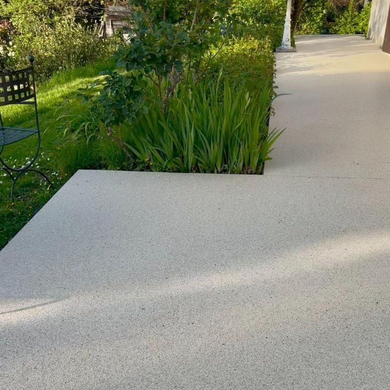 Terrasse en béton jouxtant un jardin verdoyant luxuriant, avec une chaise en métal noir sur la gauche.