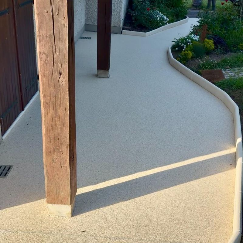 Allée de patio incurvée couleur crème, bordée de poteaux en bois et d'une bordure de jardin ensoleillée