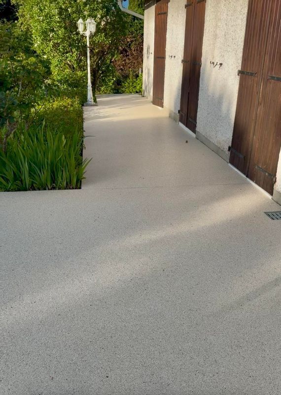 Allée en béton moderne longeant des portes en bois et des plantes vertes au soleil
