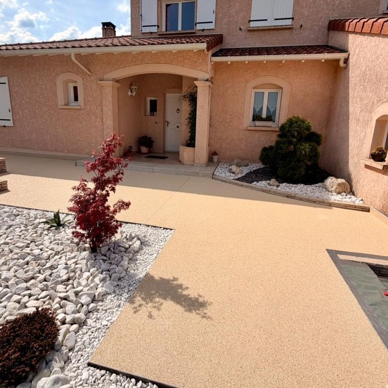 Entrée principale d'une maison couleur pêche avec une terrasse pavée beige, un aménagement paysager en pierre blanche et un petit arbuste rouge.