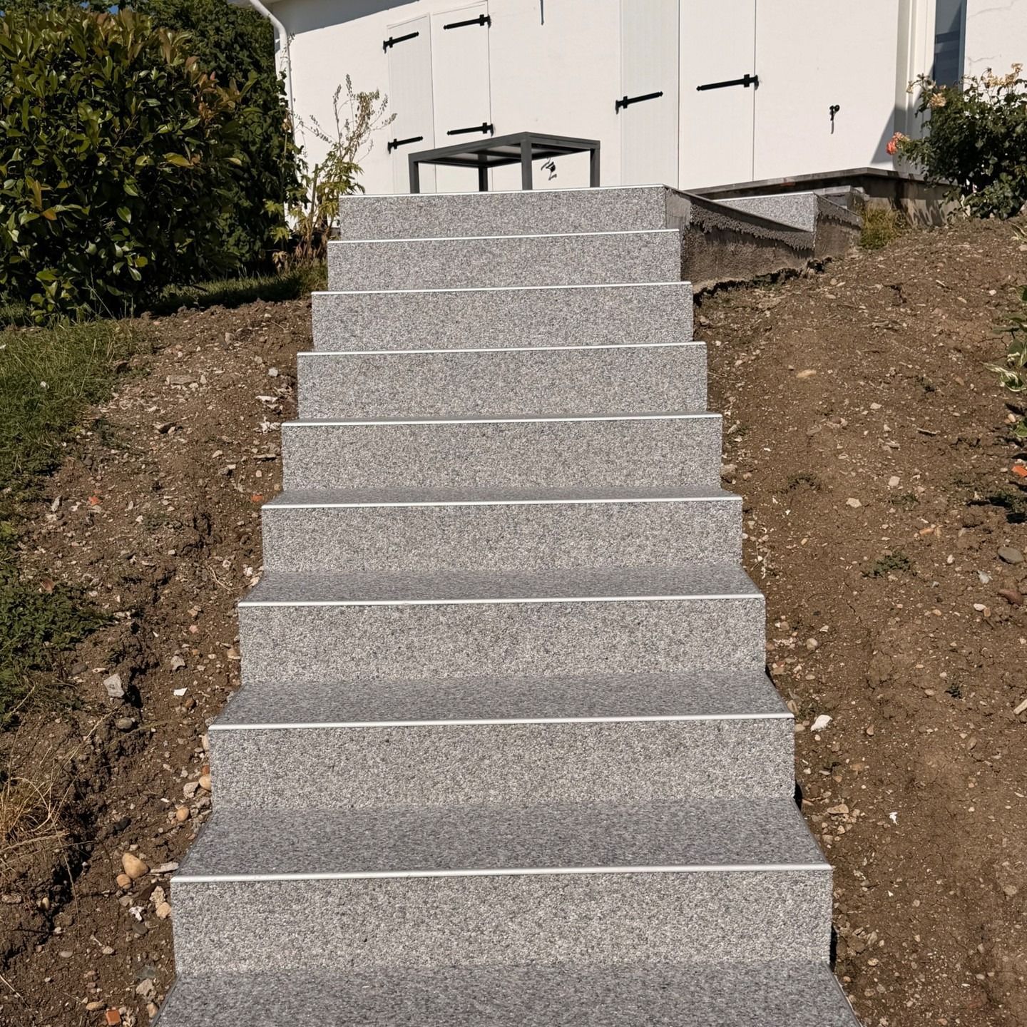 Un escalier extérieur en béton, aménagé dans un talus de terre, mène à une terrasse.