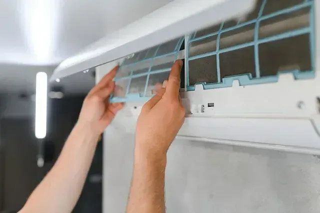 Manos reemplazando un filtro de aire acondicionado, mostrando el filtro y la unidad de aire acondicionado.