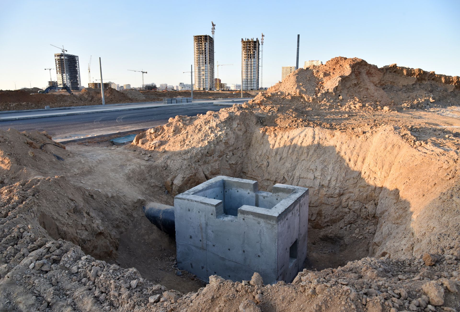 Ouvrage de drainage en béton dans une excavation à ciel ouvert. Chantier de construction avec deux tours en arrière-plan.