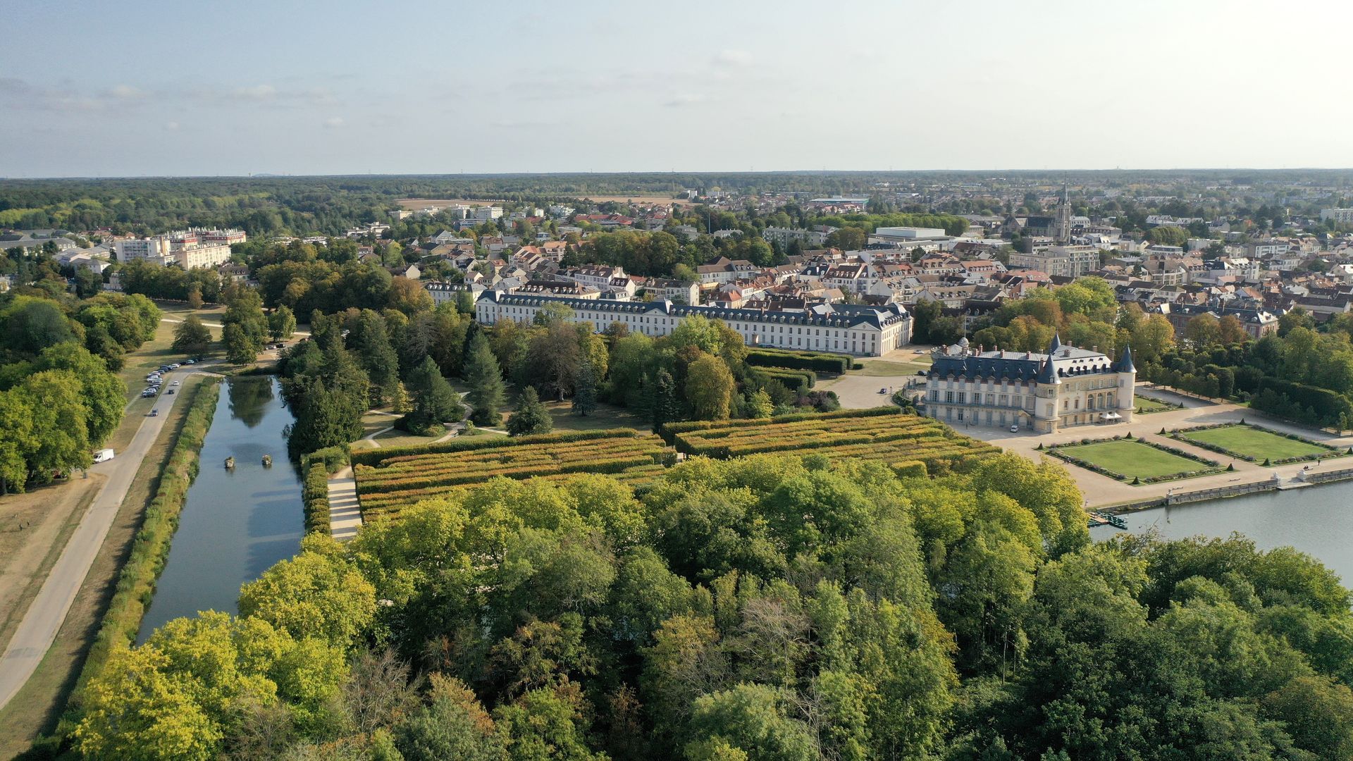 Vue aérienne de Rambouillet avec un palais, des jardins et un plan d'eau, par une journée ensoleillée.