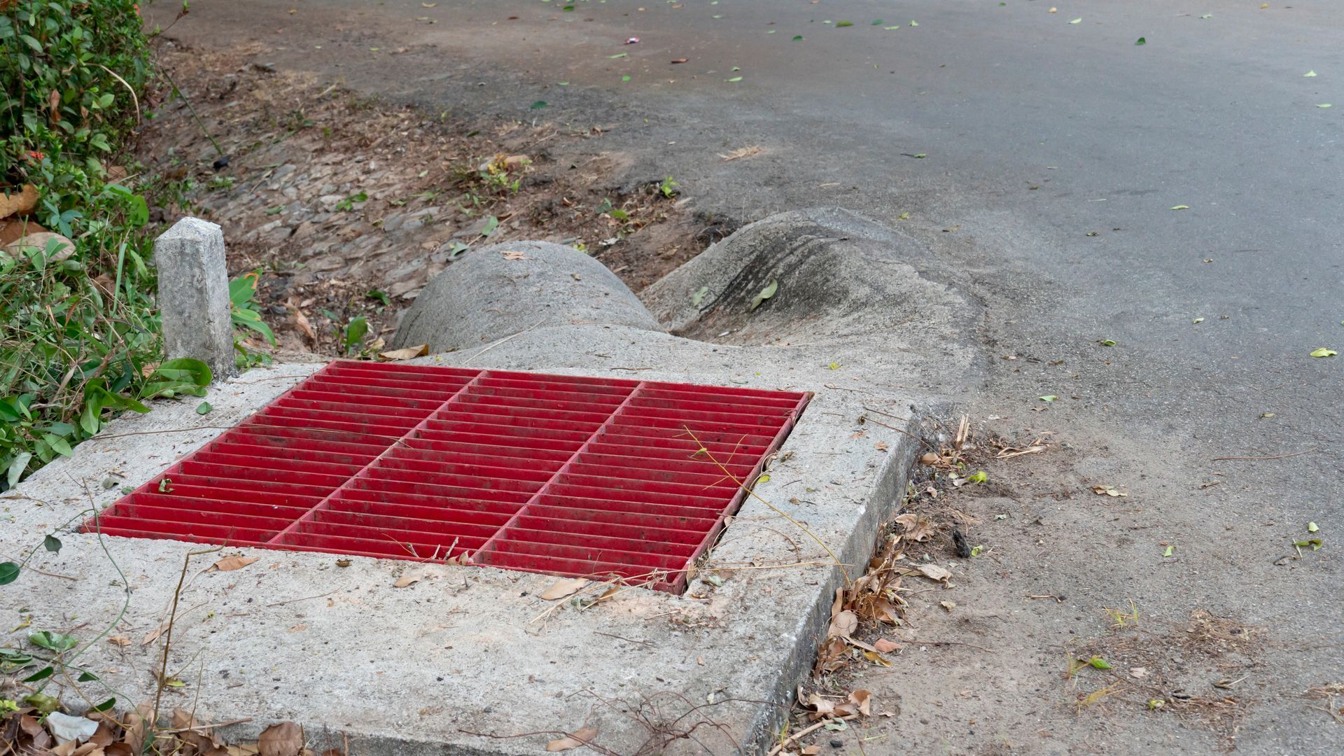 Grille métallique rouge sur béton entourant un caniveau en bord de route.
