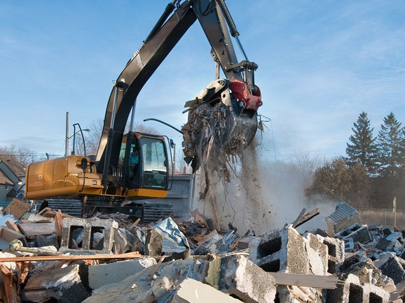 Une excavatrice concasse des débris de construction en extérieur par une journée ensoleillée.