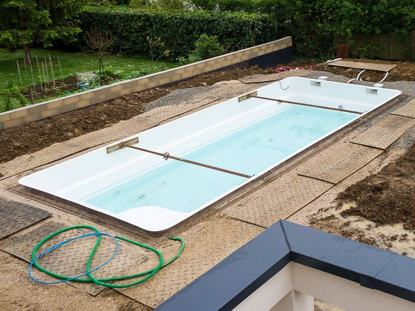 Une piscine rectangulaire en construction, entourée de gravier et de matériaux de construction, à l'extérieur.