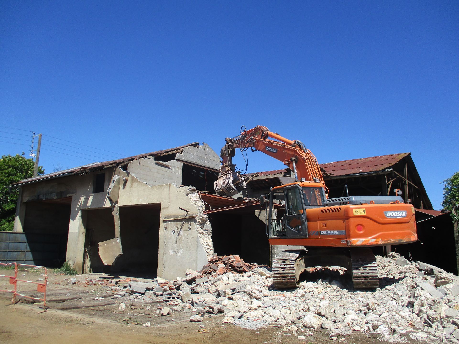 Chantier de construction avec excavatrice et ouvriers installant un système de drainage dans une cour résidentielle.