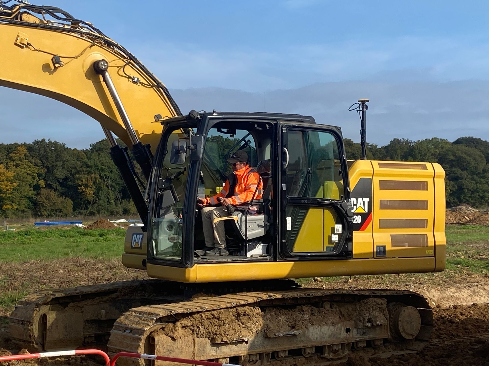 Une pelle mécanique Caterpillar jaune avec un opérateur dans la cabine sur un chantier de construction.
