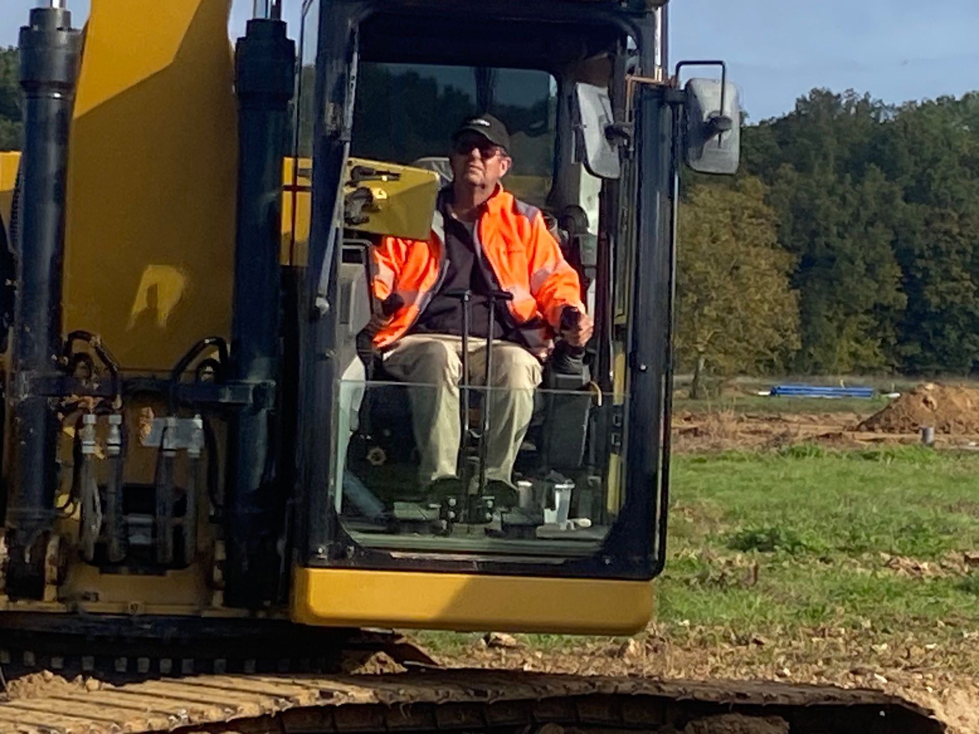 Un homme portant un gilet orange manœuvre une pelleteuse jaune sur un chantier de construction.