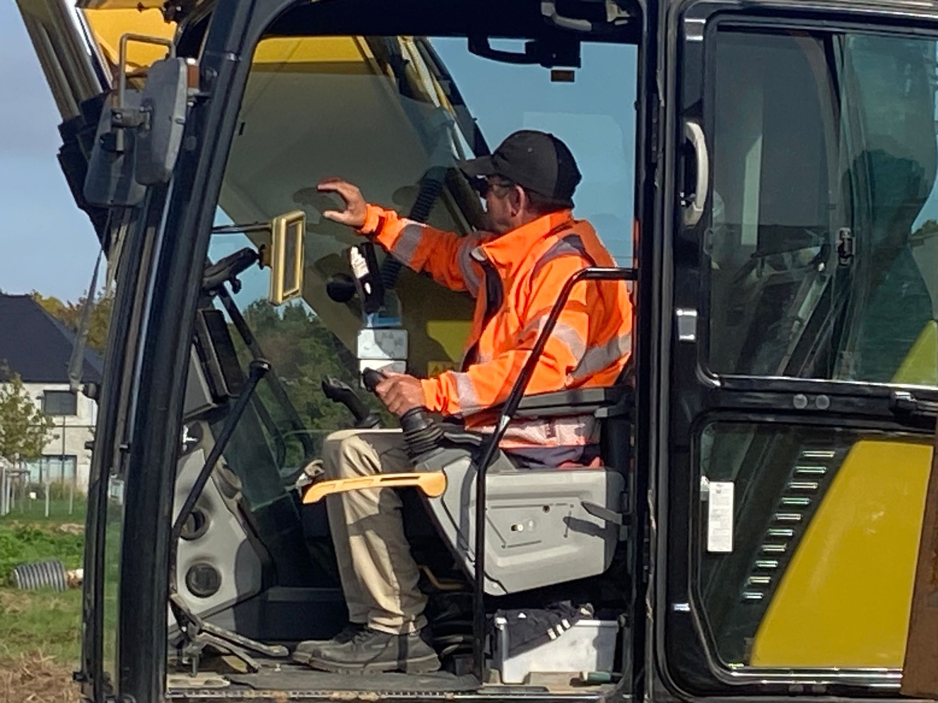 Personne portant un gilet de sécurité orange et manipulant des engins lourds sur un chantier de construction.