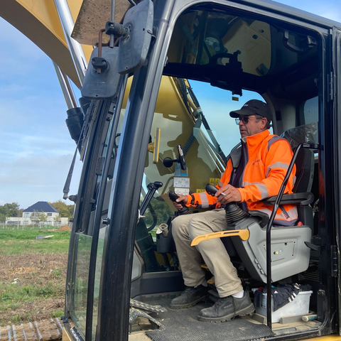 Un homme en gilet orange manœuvre une excavatrice dans un champ.