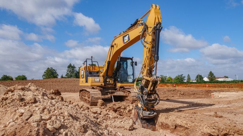 Une pelleteuse jaune creuse une fosse sous un ciel bleu nuageux.