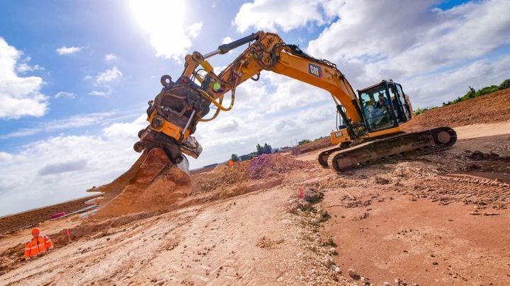 Une pelleteuse jaune équipée d'une grande lame creuse un talus de terre par une journée ensoleillée.