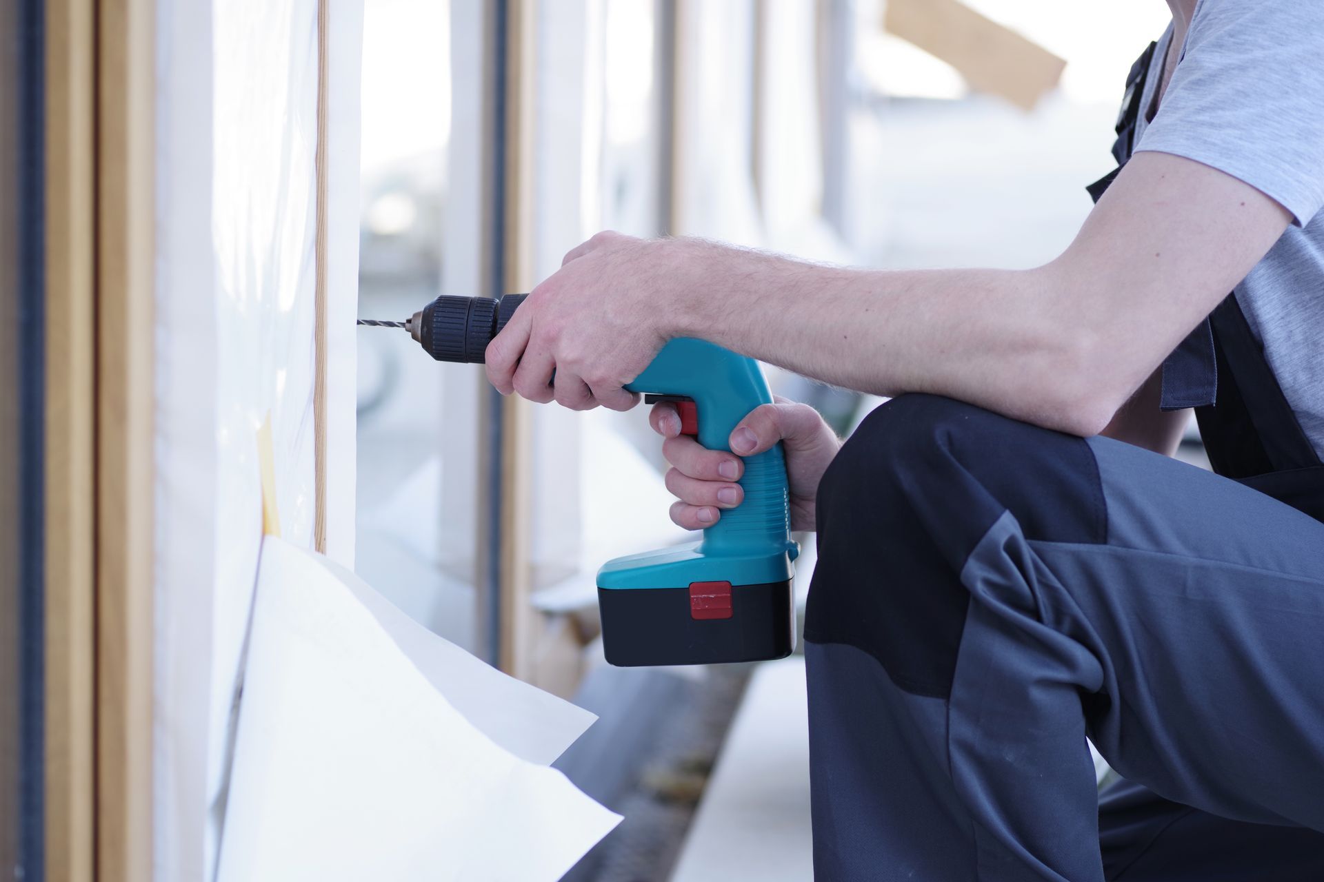 Personne utilisant une perceuse électrique bleue pour installer un cadre de fenêtre à l'intérieur.