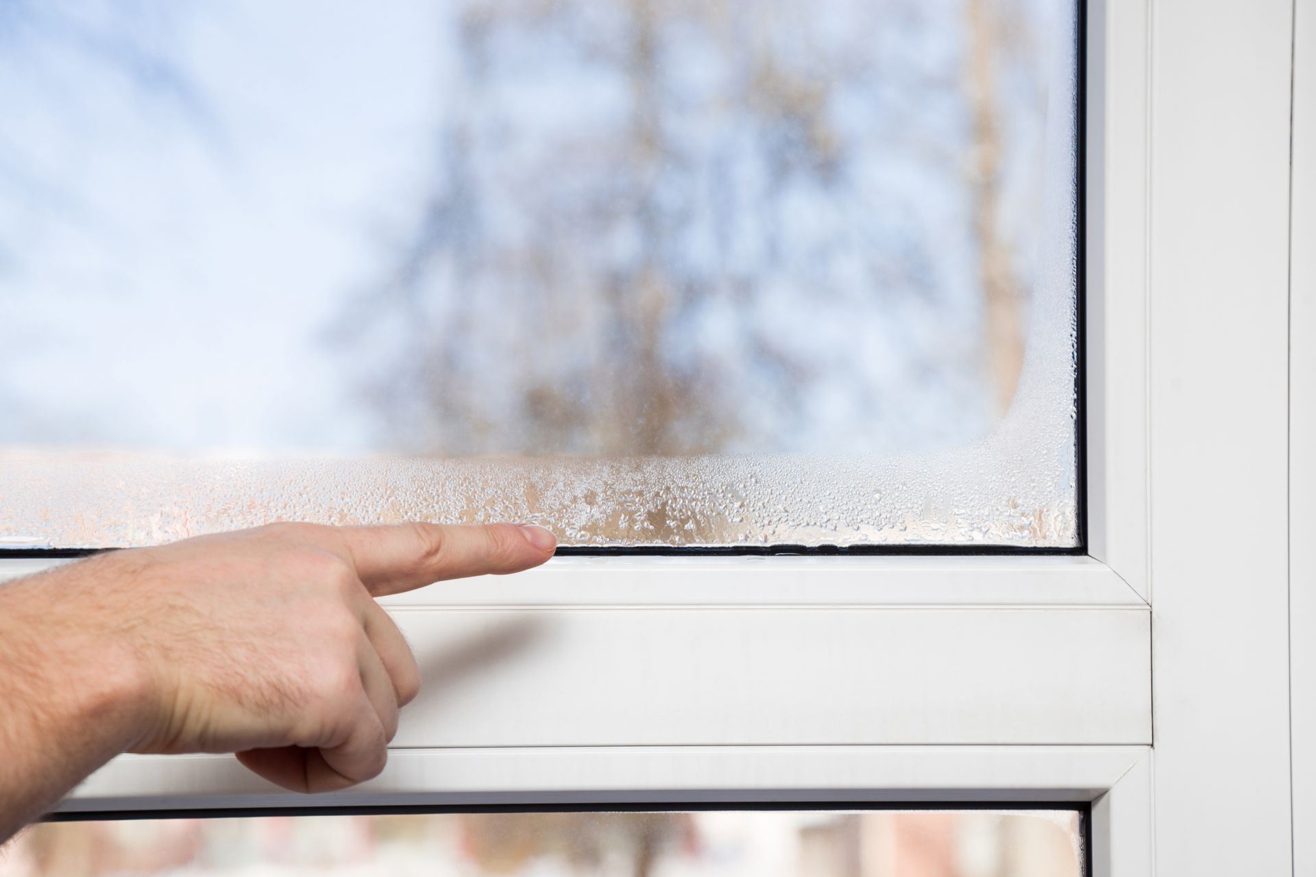 Main pointant du doigt la condensation sur une vitre dépolie.