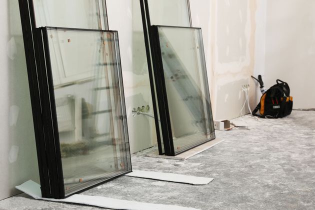 Deux grands panneaux de verre appuyés contre un mur, sur un sol recouvert de moquette, avec un sac à dos à proximité.