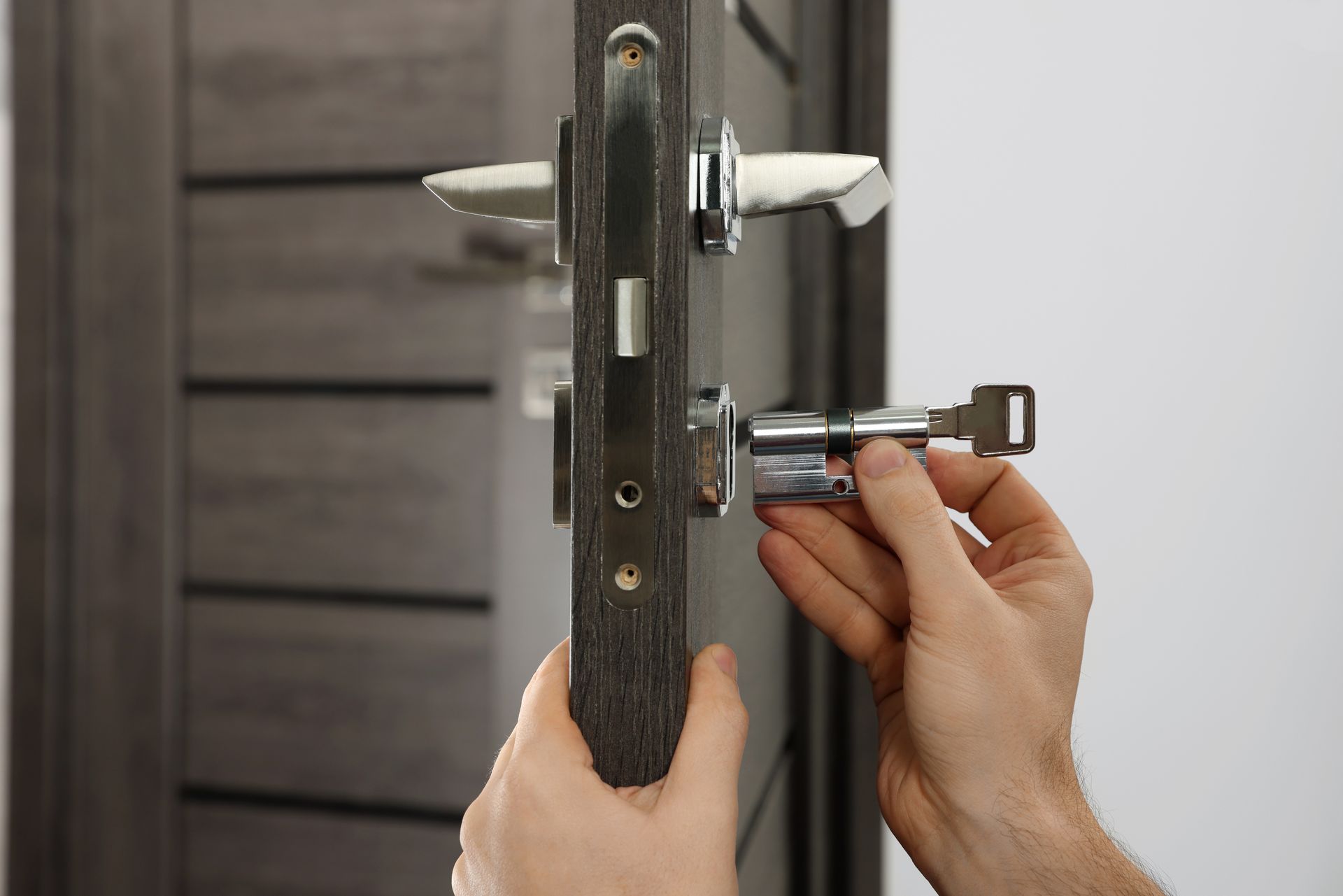 Des mains ajustent une serrure de porte avec un tournevis sur un cadre de porte gris.