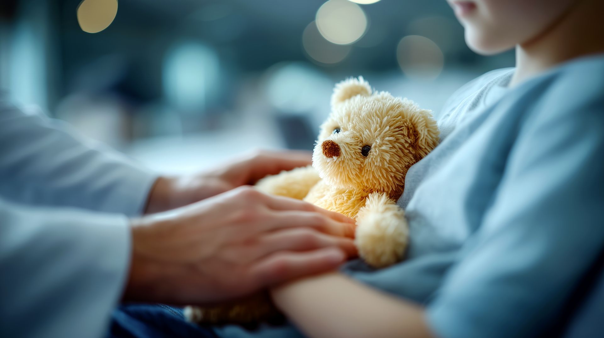 Petit ours en peluche tenu par un enfant en pyjama bleu, allongé dans un lit médical.