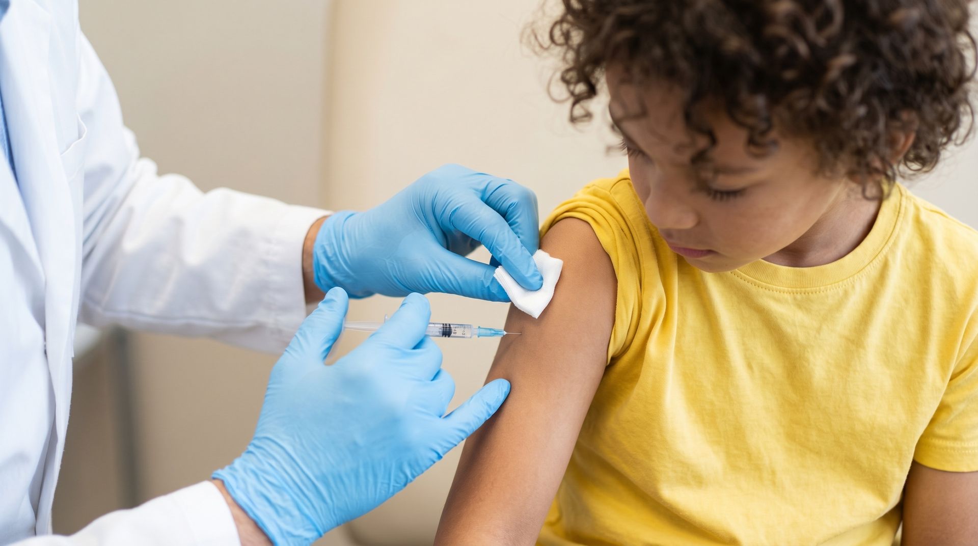 Un agent de santé administre une injection à un enfant portant une chemise jaune