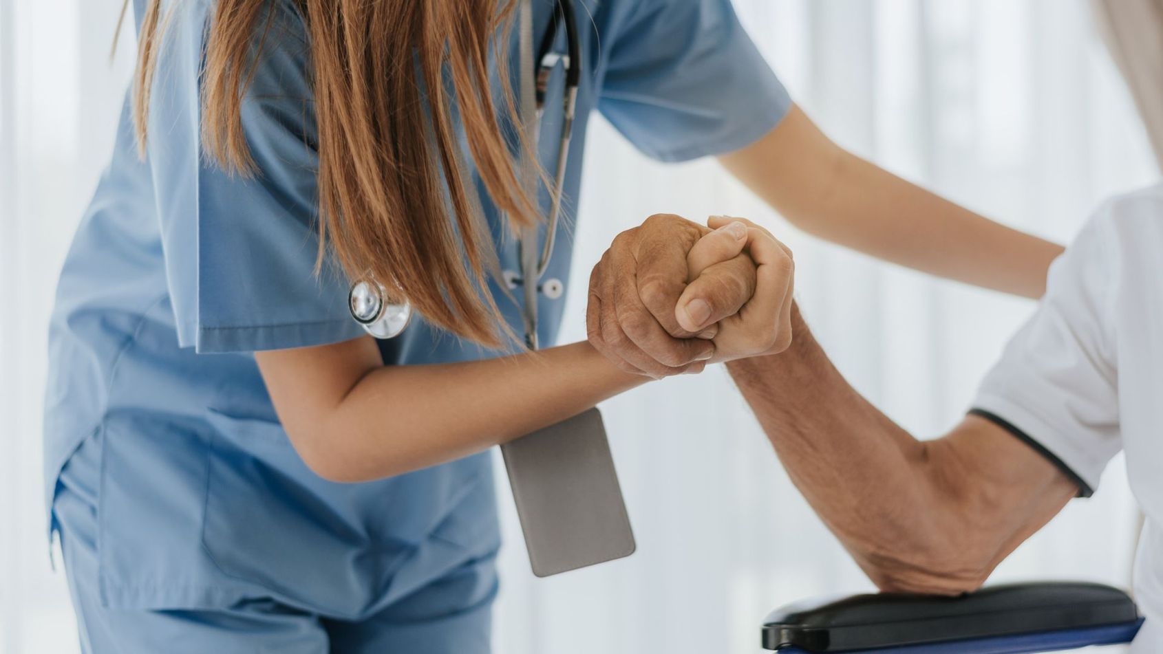 Une infirmière aide un patient en lui tenant la main, dans un environnement clinique lumineux