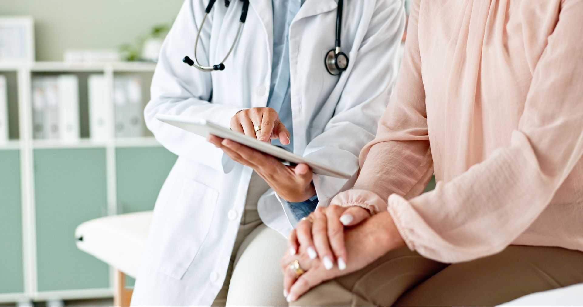 Un médecin consulte un patient assis et lui montre des informations sur une tablette dans une salle de consultation lumineuse.