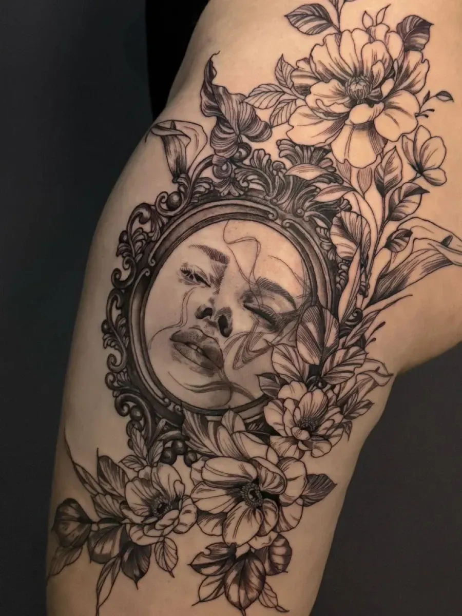 Tatuaje floral en negro y gris de un rostro de mujer en un brazo, con flores enmarcando el diseño