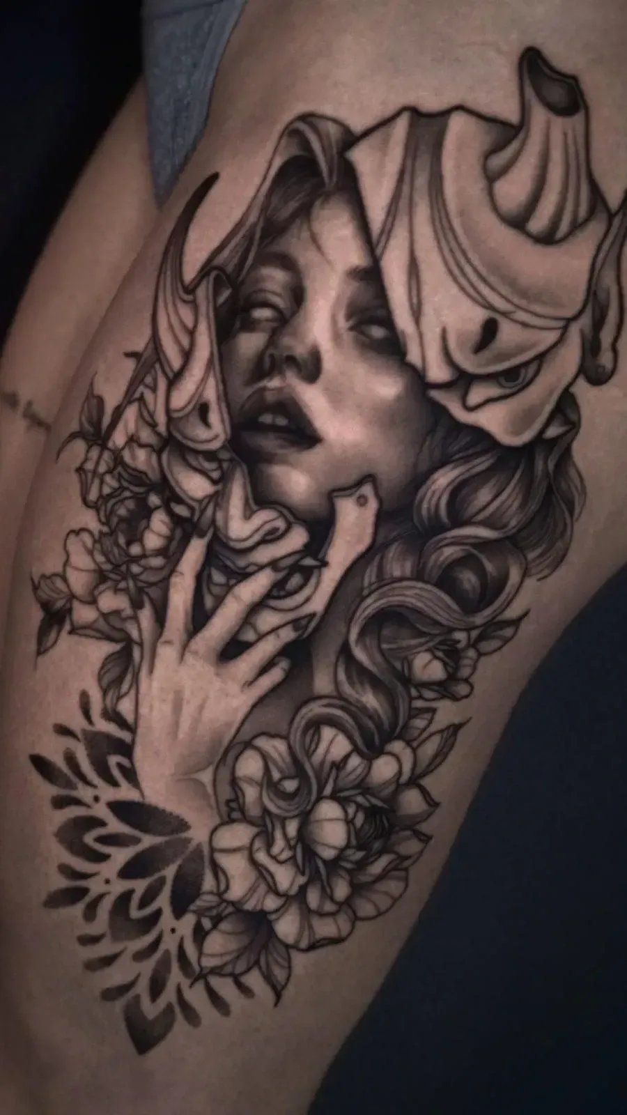 Tatuaje en el muslo, en negro y gris, con el rostro de una mujer, rosas y volutas decorativas