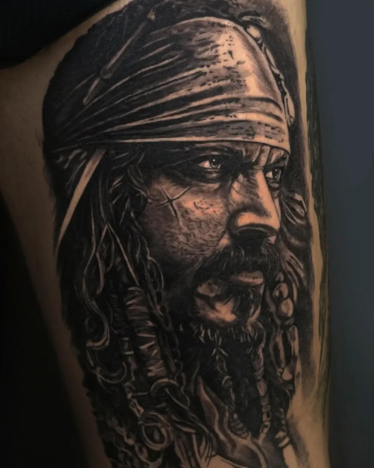 Tatuaje de estilo retrato en negro y gris de un pirata barbudo con un pañuelo en la cabeza, de perfil