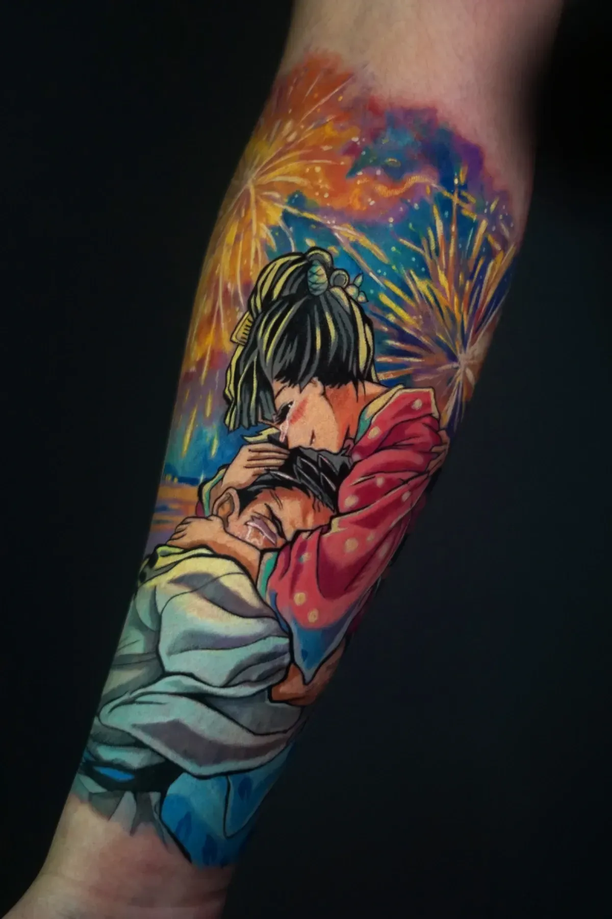 Tatuaje colorido en el antebrazo de un abrazo con fuegos artificiales y vibrantes tonos azules, rojos y dorados